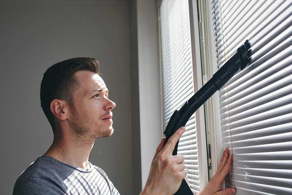 man vacuuming blinds